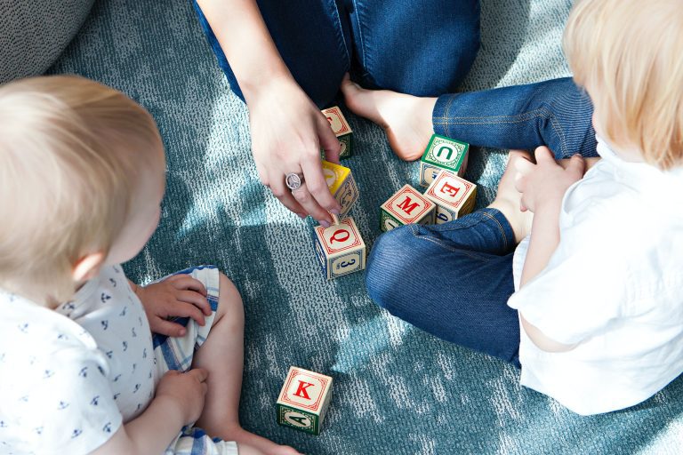 two toddlers and a parent or teacher playing with letter blocks